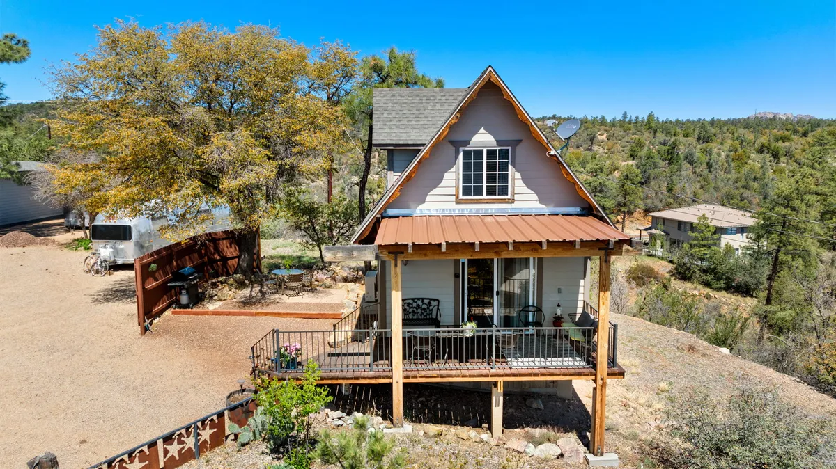 The front porch of the property, framed by a wooden railing and surrounded by abundant greenery with a mountain view beyond. The inviting porch suggests a seamless transition between indoor comfort and outdoor adventure.