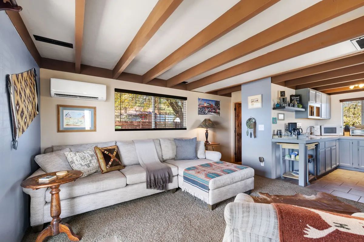 This image captures an inviting living space featuring a comfortable sofa, a coffee table, and a glimpse of the adjoining kitchen area. Warm artwork adorns the walls, and soft lighting enhances the cozy, communal mood. The overall composition emphasizes a space ideal for relaxing, socializing, or enjoying a quiet evening in.