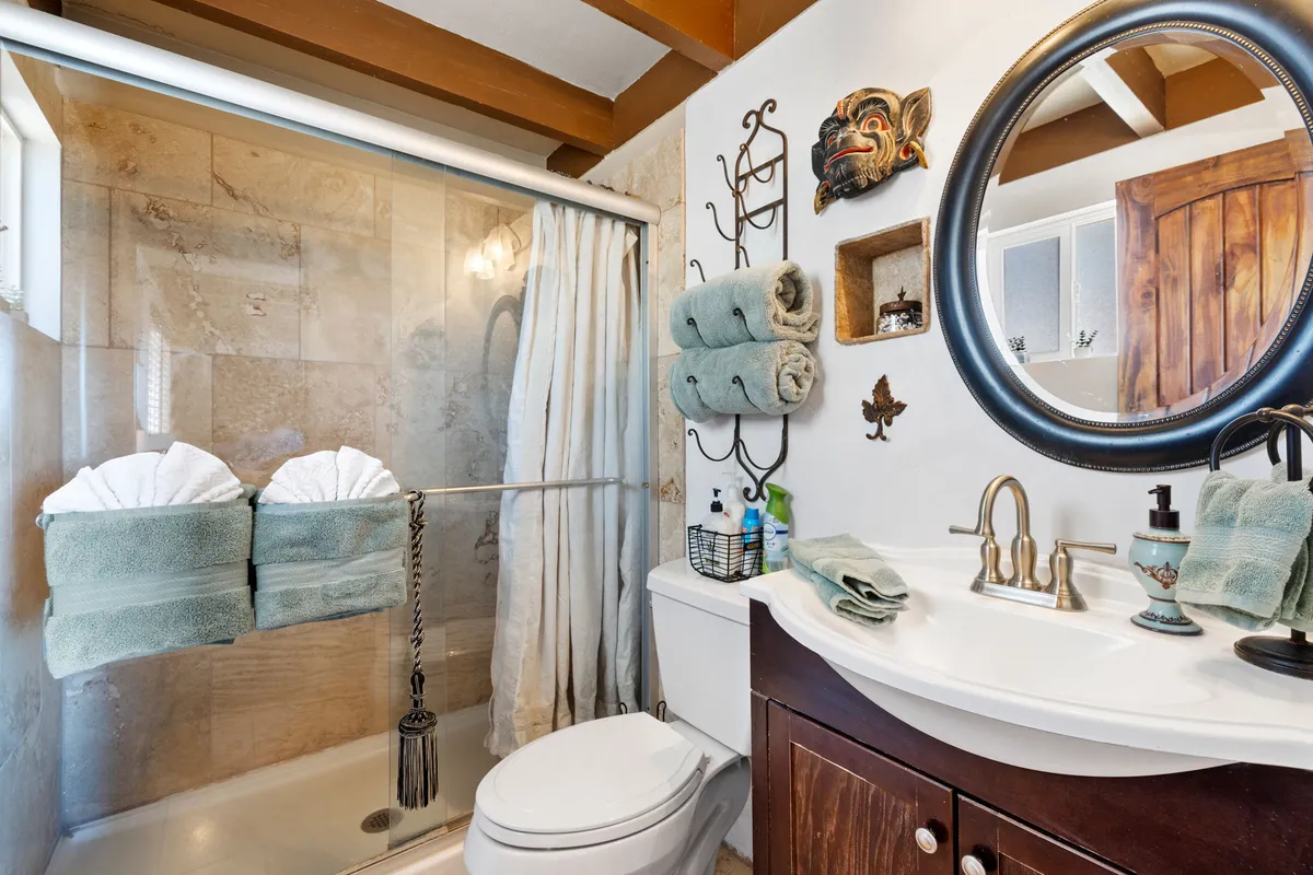 A bathroom interior showcasing a refreshing shower area, a well-lit vanity with decorative wall art, and stacks of fresh towels. The space feels tranquil and thoughtfully appointed with essential amenities.
