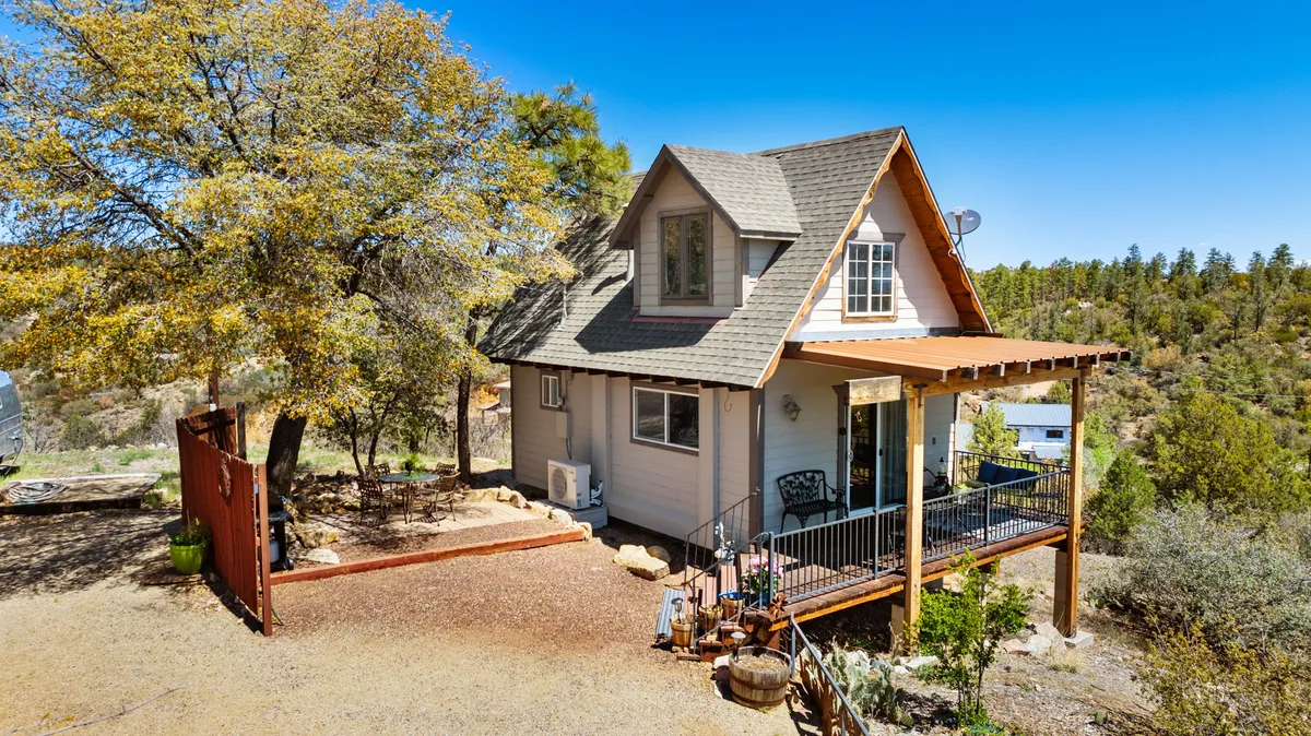 The hero image shows a charming chalet nestled among tall pines, with a welcoming porch overlooking the scenic mountain landscape of Prescott's Thumb Butte. The cozy exterior invites guests to relax outdoors, take in stunning sunsets, and enjoy the tranquility of the surrounding nature.