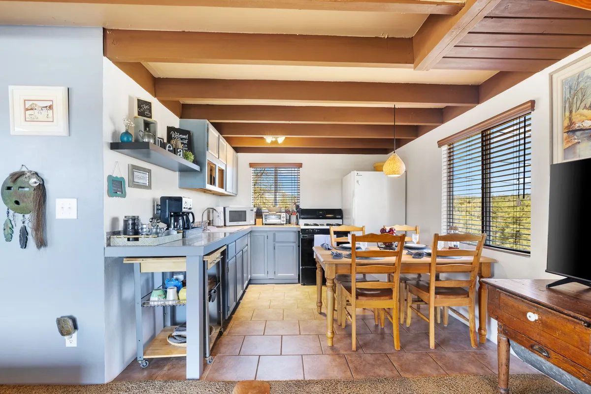 A welcoming view of a kitchen and dining area, featuring a farmhouse dining table set near windows that overlook the forest. The kitchen showcases modern appliances, spacious counters, and warm lighting, with ample room for cooking and socializing.