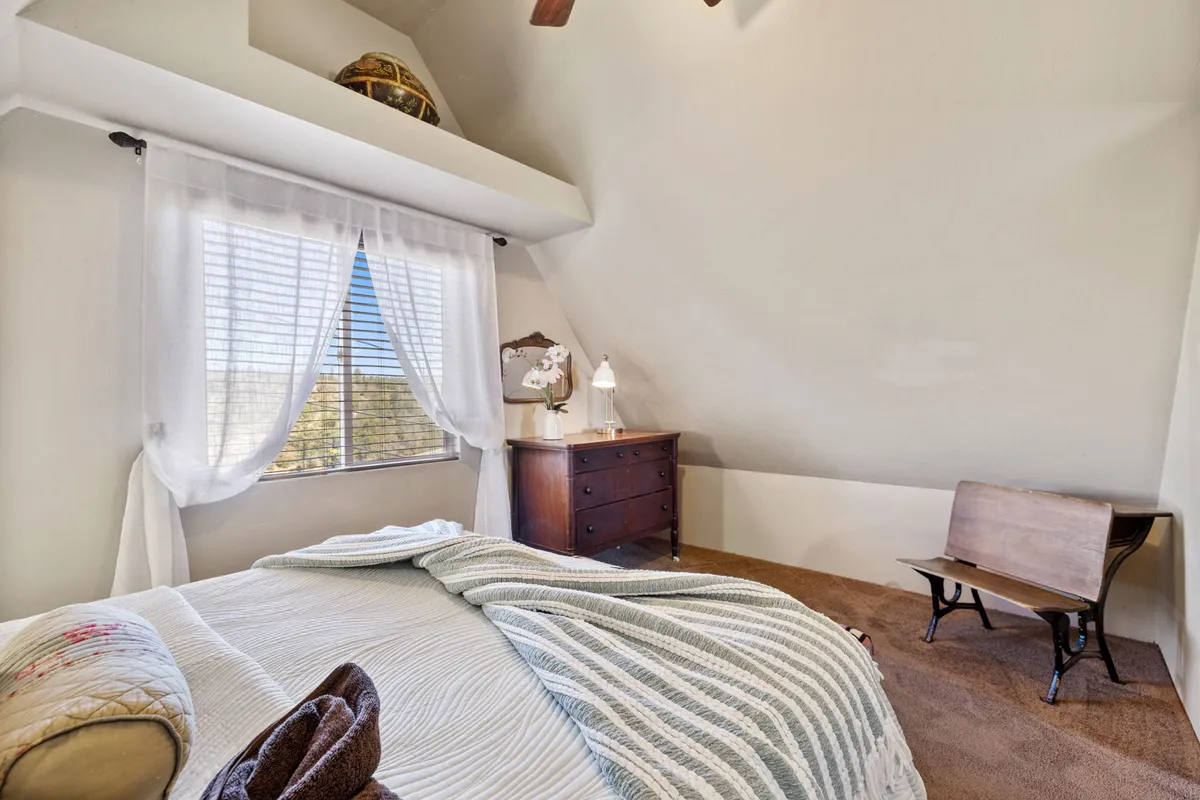 A tranquil bedroom scene featuring a bed with a striped blanket, a wooden dresser, a vintage mirror, and a window draped with sheer curtains. Soft, natural light filters into the room, creating a peaceful and restorative atmosphere.