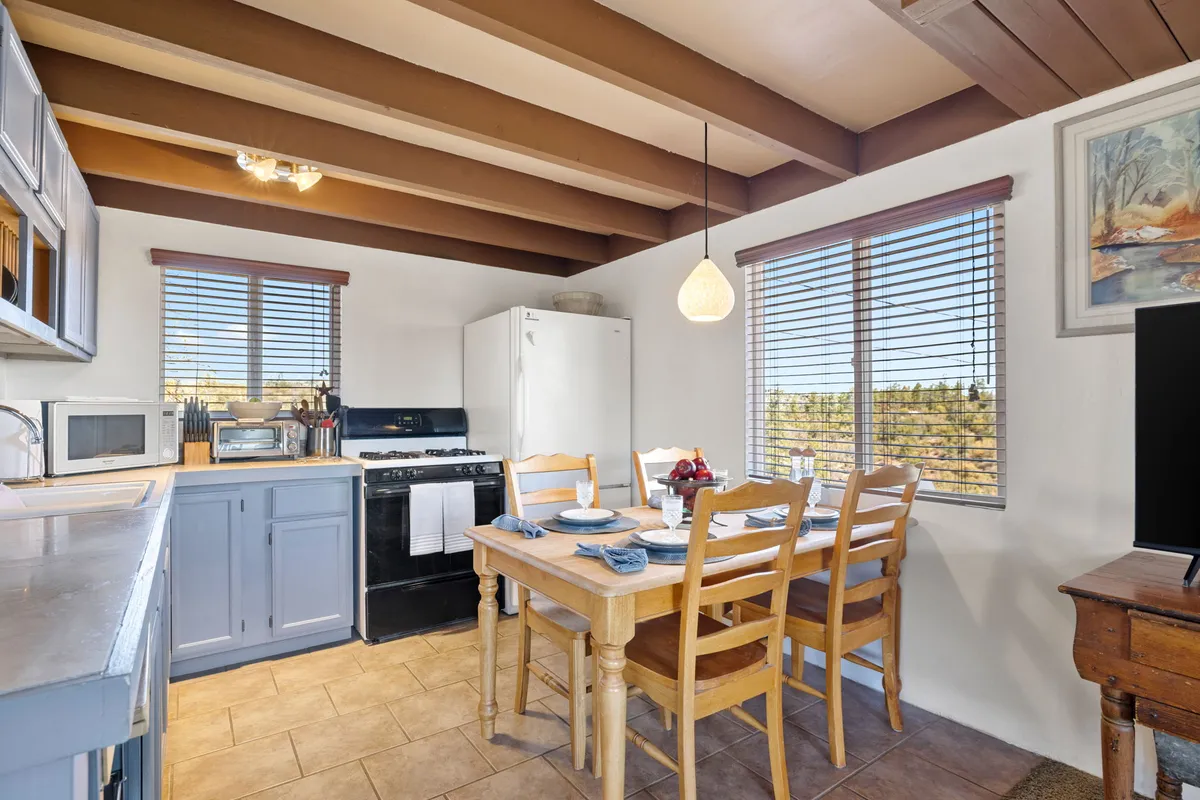 A bright, airy open kitchen and dining space with a dining table elegantly set for a meal. Stainless steel appliances and countertops are visible, along with natural light streaming in through the windows. The overall mood is one of warmth and togetherness.
