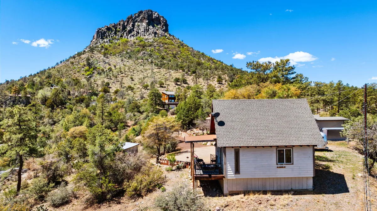 This exterior image captures the chalet nestled among tall trees with a prominent mountain rising in the background. The setting radiates tranquility, with visible trails leading toward the forest, suggesting immediate access to hiking and nature right from the property. The porch and surrounding area evoke relaxation and a strong connection to the outdoors.