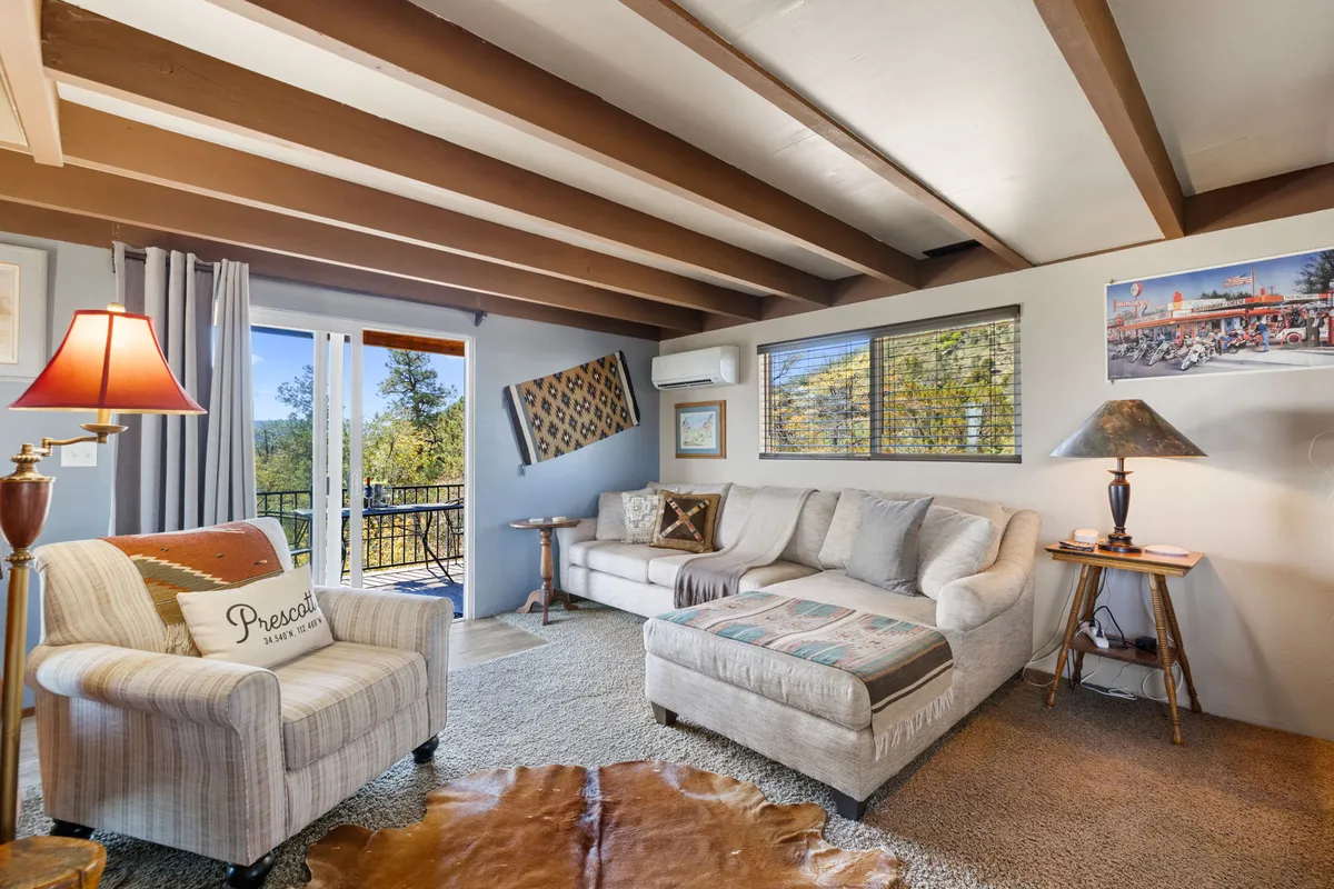 A snug corner of the living room is shown with a plush sofa and an armchair facing a window, accentuated by a soft lamp and tasteful artwork. The arrangement invites relaxation, reading, or intimate conversation, while the window likely frames the scenic mountain views mentioned in the text.