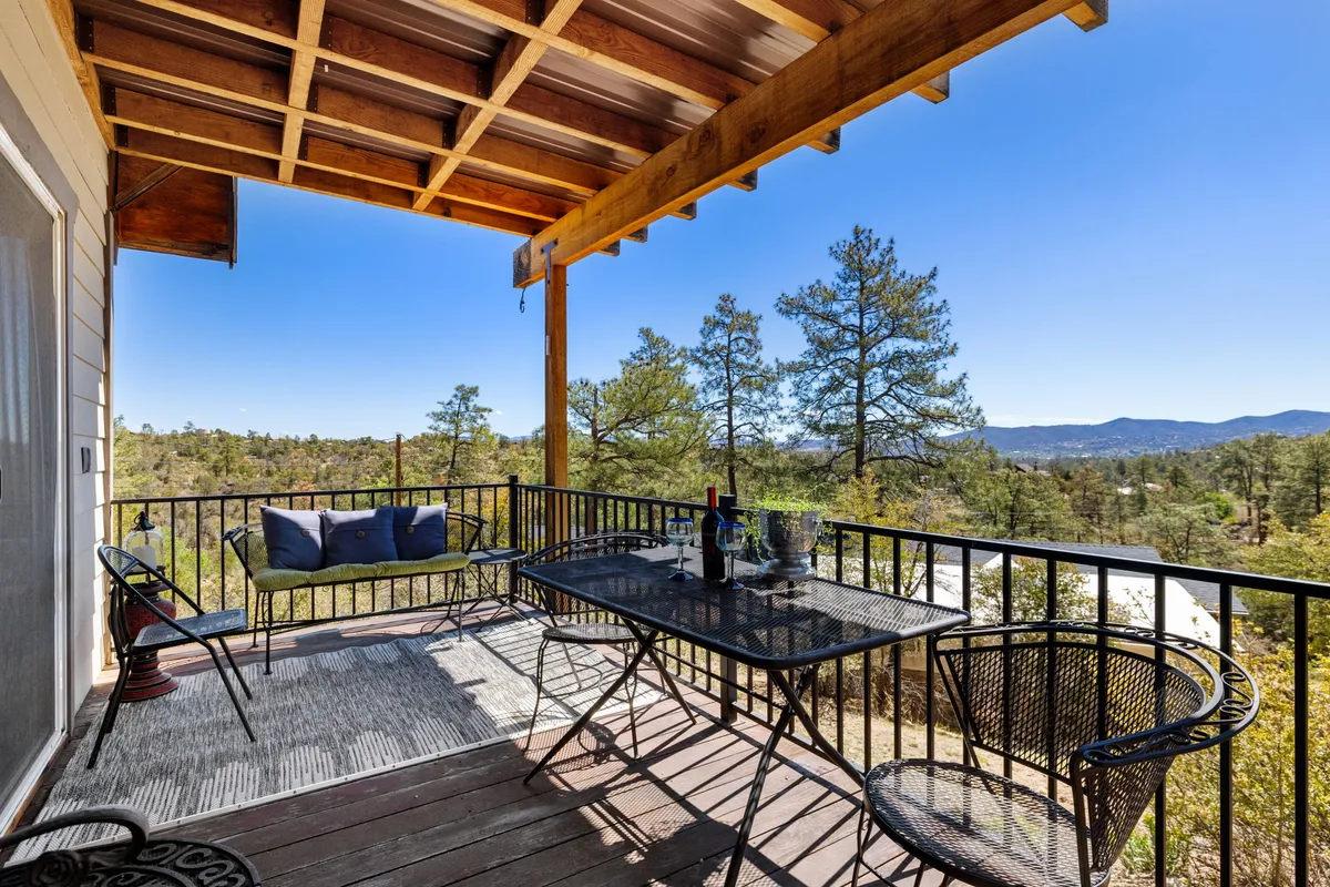 An exterior view focusing on an inviting outdoor seating area with a table set for wine and relaxation. The backdrop includes sweeping views of the landscape, framing a tranquil scene for savoring drinks, unwinding with friends, or taking in sunsets and morning mist.